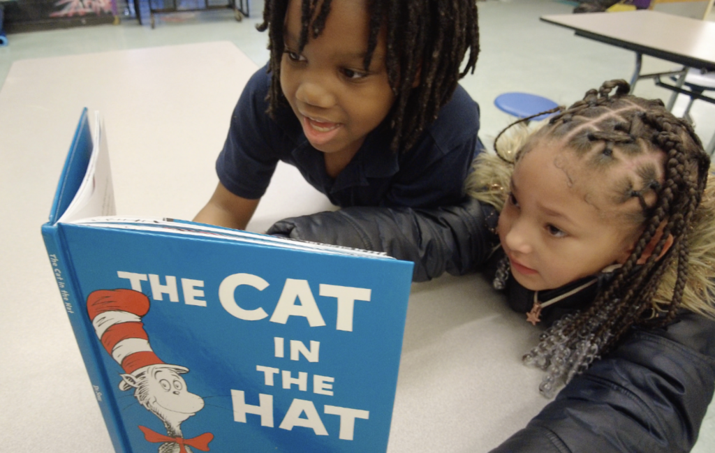 Two children at a table reading "The Cat in the Hat" by Dr. Seuss.